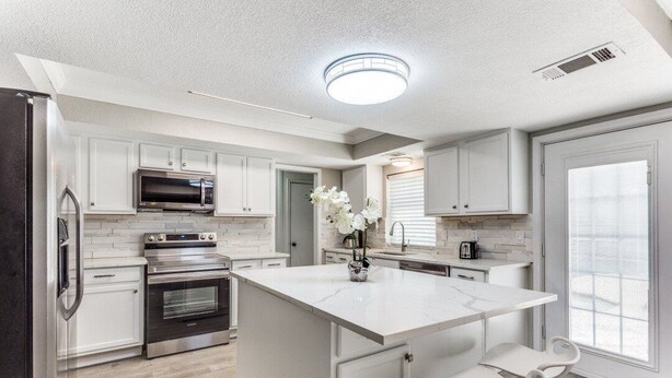 A modern kitchen with white cabinetry, a central island with seating, a built-in oven, and a microwave. - Reston NEW Bright, Airy Home w/ In Ground Pool & Grill (Richardson)