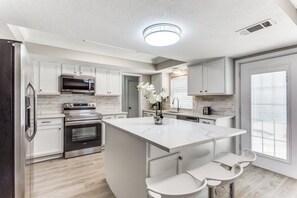 A modern kitchen with white cabinetry, a central island with seating, a built-in oven, and a microwave.