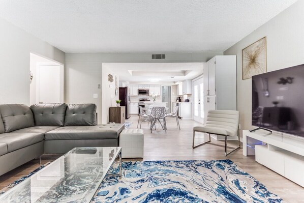 A modern living room with a sectional sofa, a glass coffee table, and a TV on a white stand.