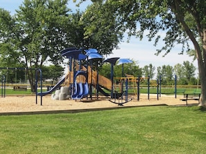 A playground with slides and swings, surrounded by grass and trees. - Large home with yard, 7 bedrooms, and lots of living space (Huron)