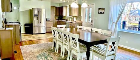 A spacious kitchen with modern appliances, a dining area with a large table and chairs, and a view through a window.