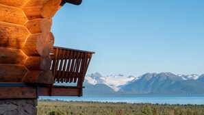 A wooden cabin with a balcony overlooking a lake and mountains.