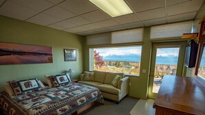 A bedroom with a large bed, a sofa, a desk, and a view of mountains.