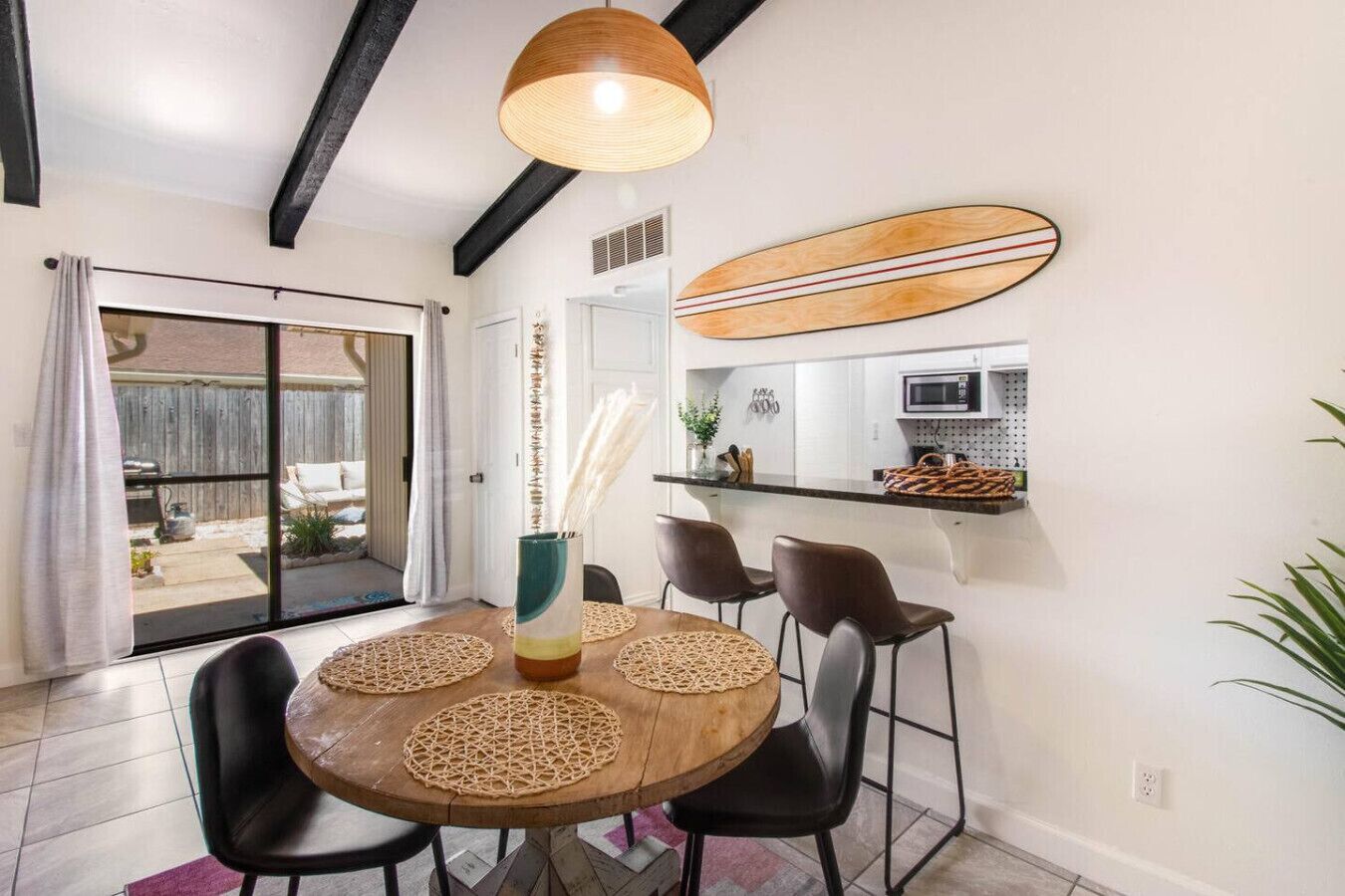 Un coin repas avec une table ronde en bois, des chaises noires, un luminaire suspendu et une décoration murale représentant une planche de surf.