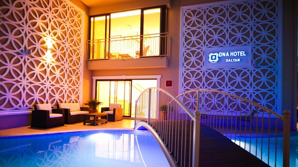 An indoor swimming pool with a geometric wall design, a lounge area with seating, and a sign for DNA Hotel Dalian. - Dna Hotel Dalyan Adult Only (Ortaca)