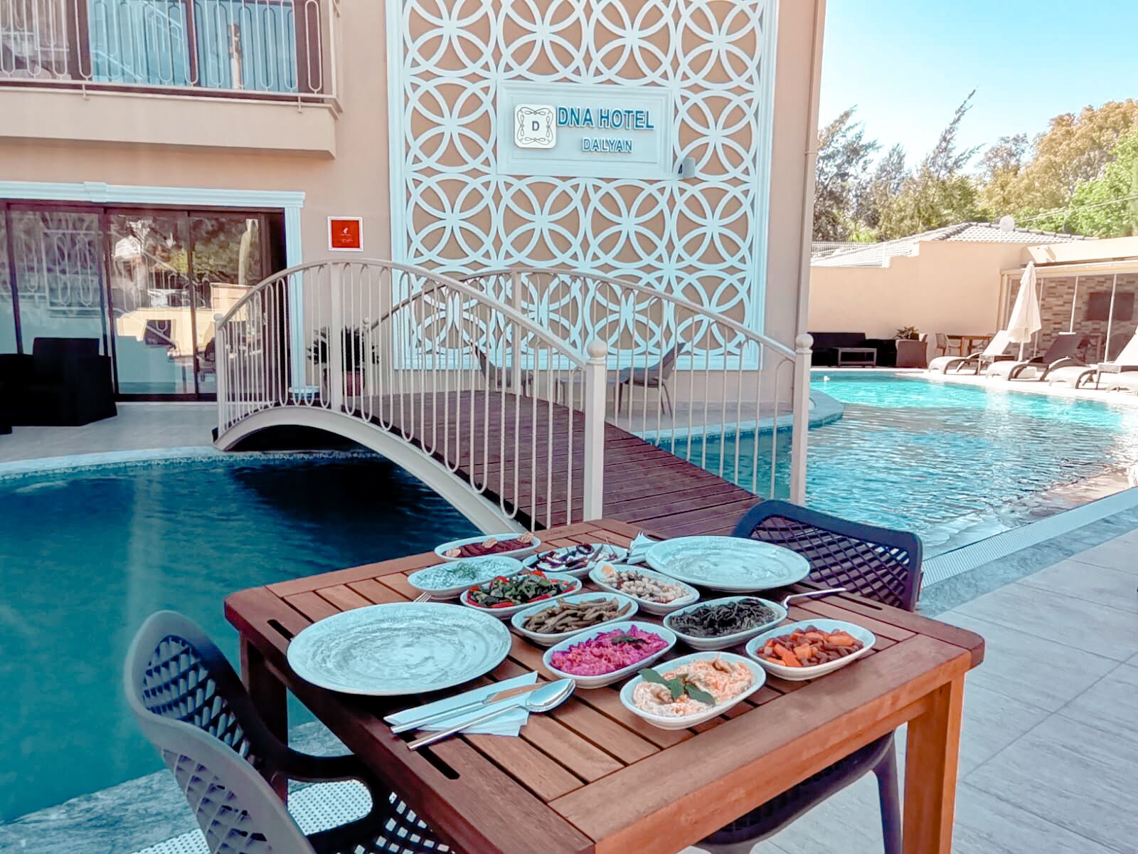 A poolside dining area with a table set for a meal, surrounded by lounge chairs and a pool.