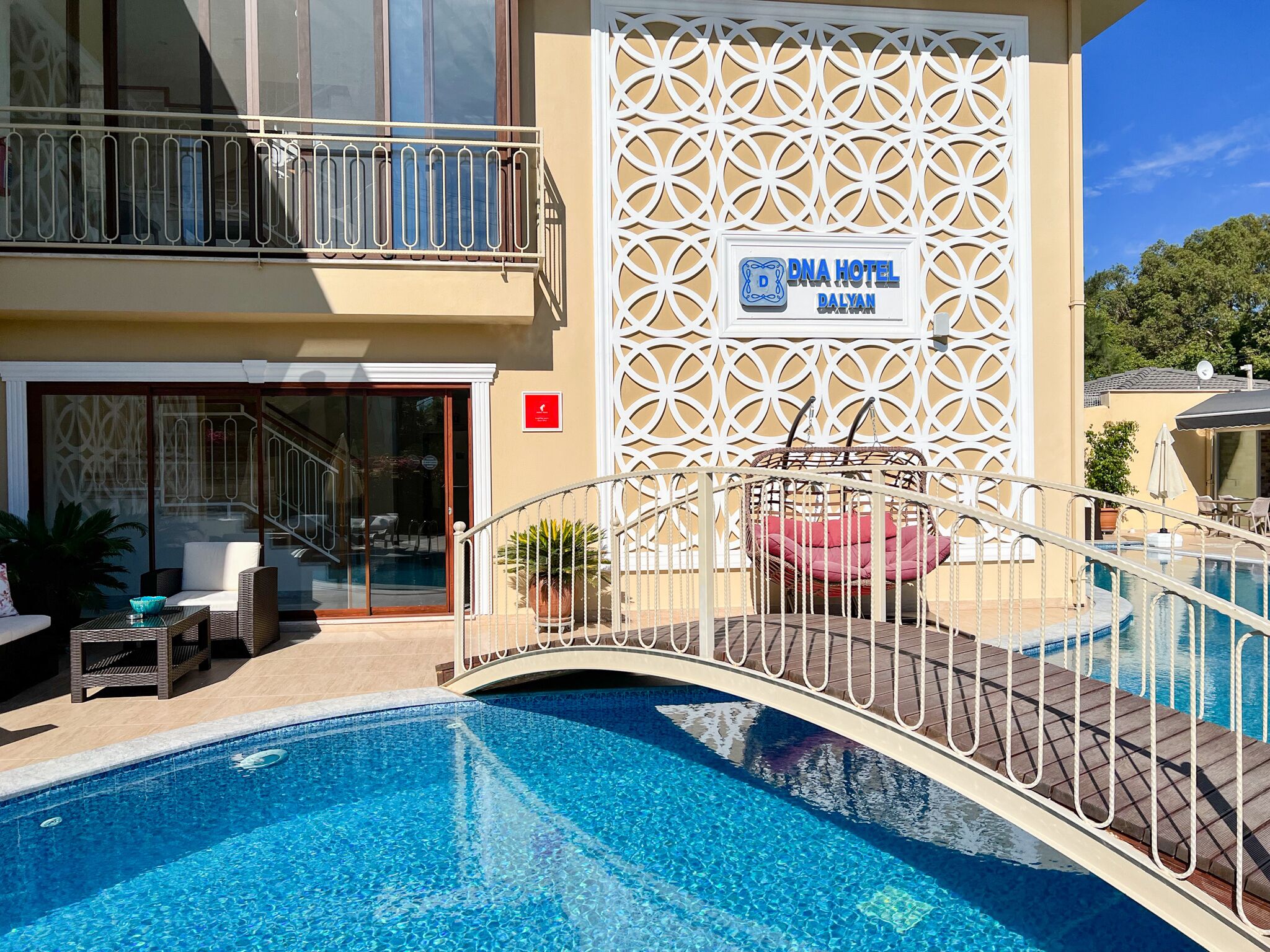 Un hotel con piscina, mobiliario exterior y una pared decorativa.