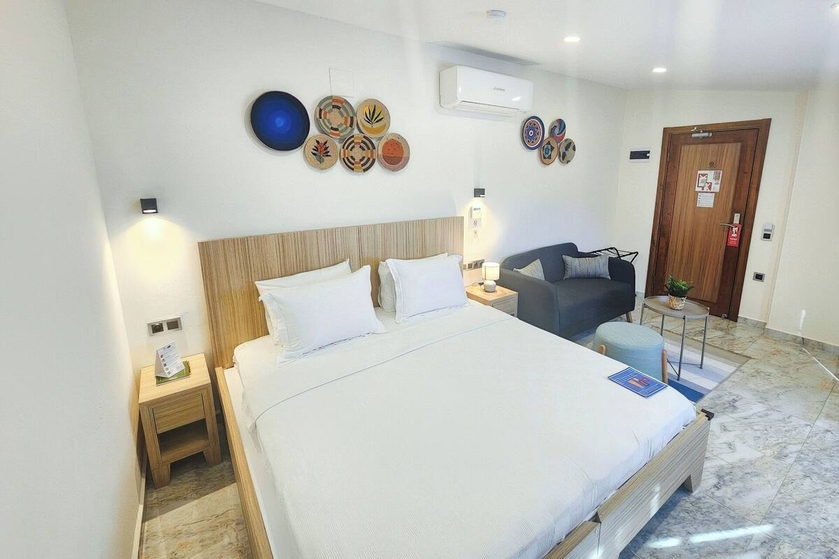 A hotel room with a large bed, a sofa, a small table, and a door.