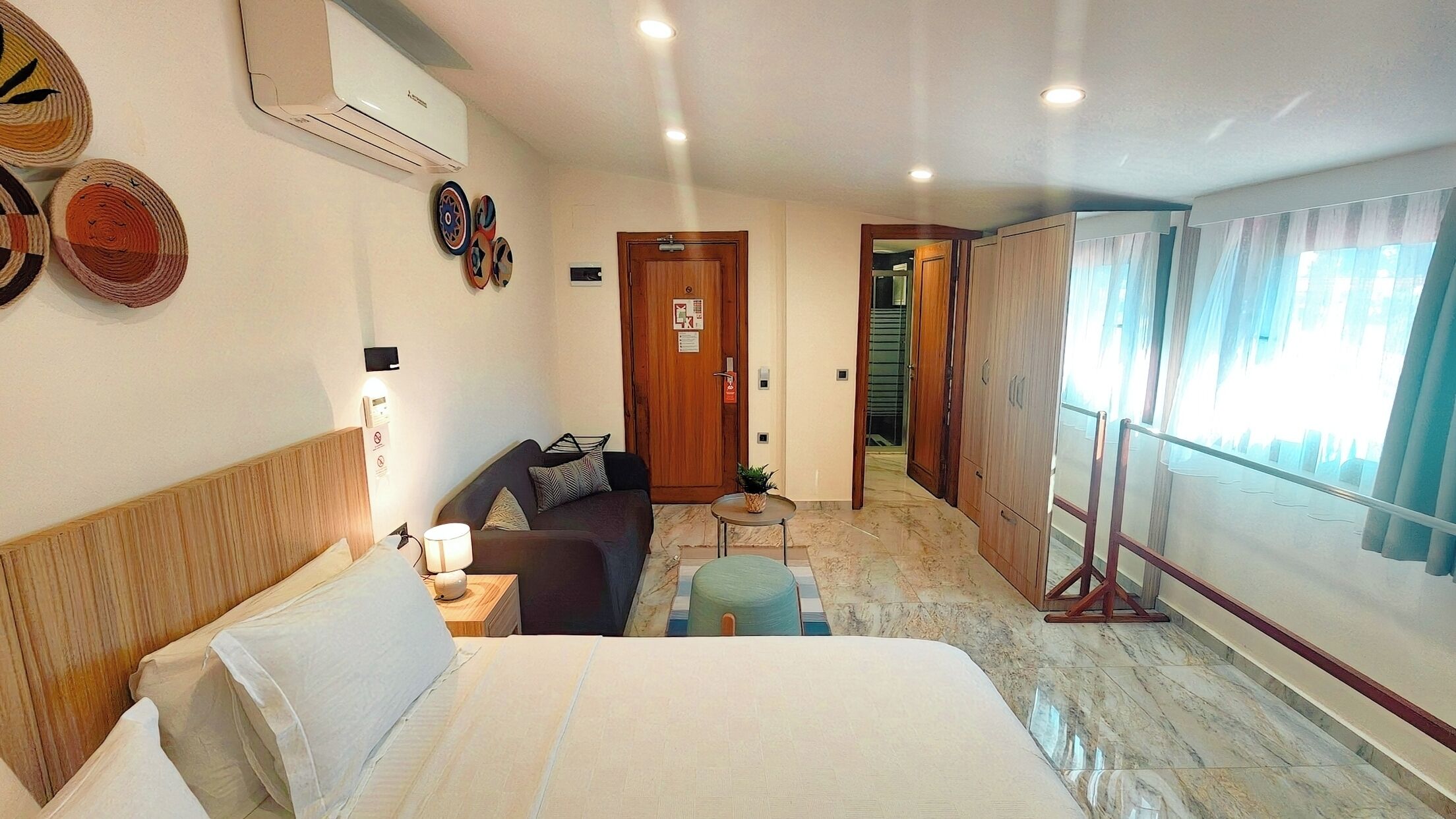 Una habitación de hotel con cama, sofá, una mesita y una ventana con cortinas.