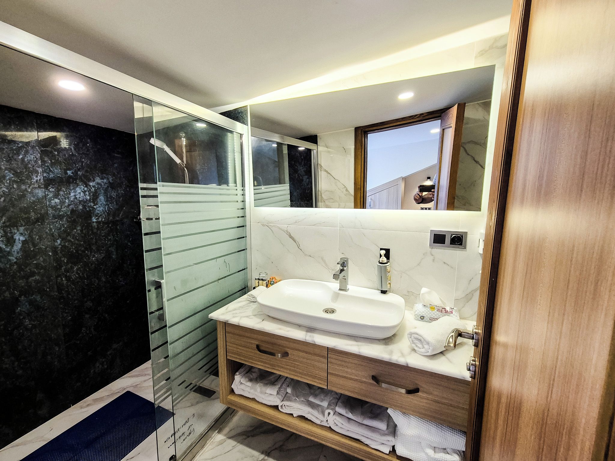 Un baño moderno con cabina de ducha de vidrio, un lavamanos blanco y baldosas de mármol.