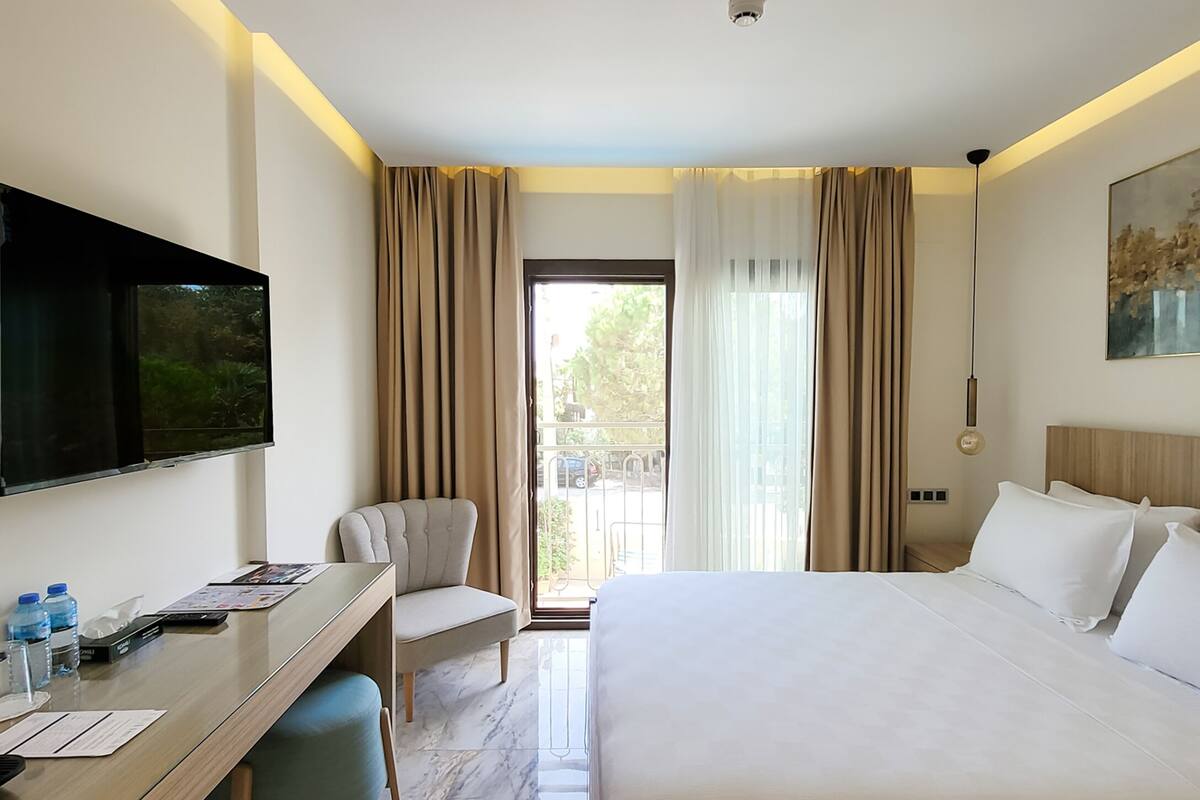 A hotel room with a bed, a desk, a chair, a TV, and a window with curtains.