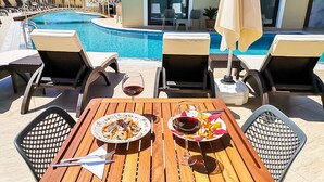 A poolside dining area with a table set for two, two plates of food, and two glasses of red wine. - Dna Hotel Dalyan Adult Only (Ortaca)