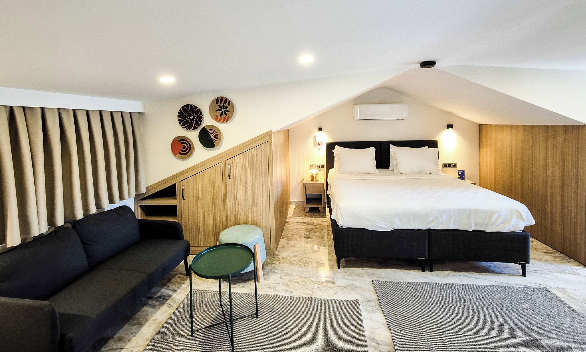 Un dormitorio con una cama, un sofá, una silla, una mesita de noche y una pared decorada con placas.