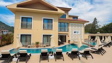 A hotel with a pool, multiple lounge chairs, and a mountain backdrop.