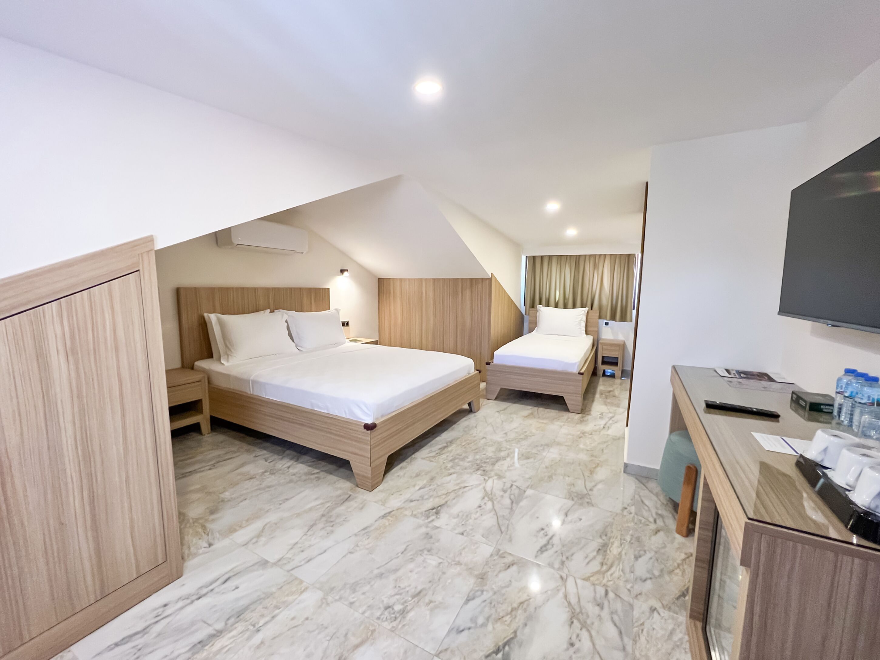 A hotel room with two beds, a desk, a TV, and a minibar.