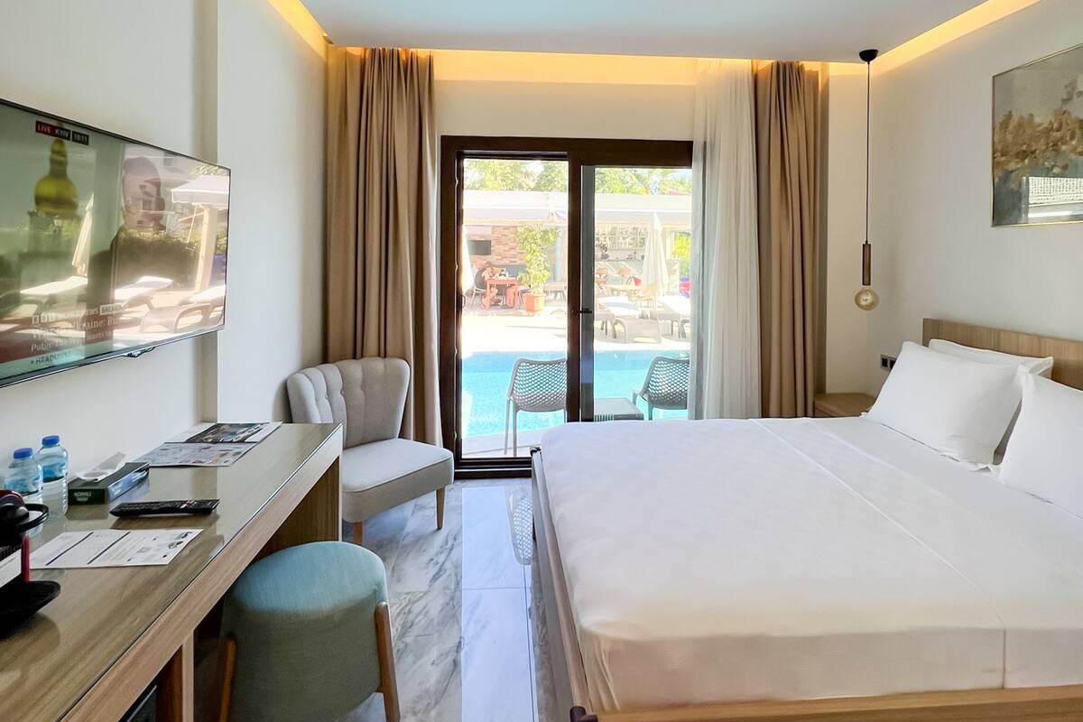A hotel room with a bed, desk, chair, and a view of the outdoor pool area.