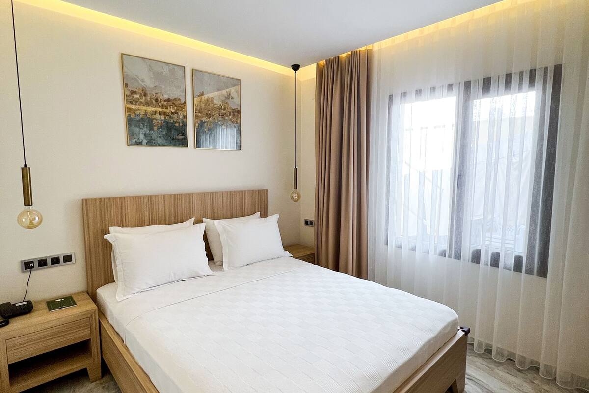 A neatly made bed with white linens, a wooden headboard, and two wall-mounted paintings.