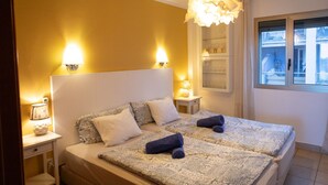 Un llit doble amb roba de llit estampada, dues làmpades de nit, una làmpada penjant decorativa i una vista d'un balcó a través d'una finestra.