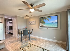 A modern living room with a dining area, a ceiling fan, a TV on the wall, and a view of the ocean. - *Special* Walk to Beach-1bd-1ba-2 Pools-2 Hot tubs (Galveston)