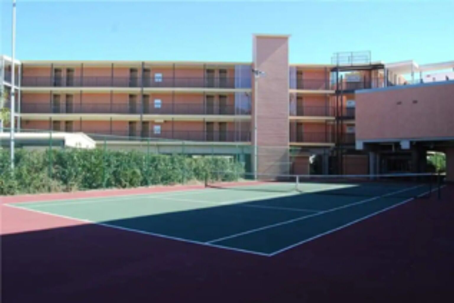 An outdoor tennis court adjacent to a multi-story building with balconies.