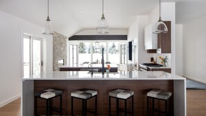 A modern kitchen with a large island, bar stools, pendant lighting, and a view of the outdoors. - Sweeping Teton views, modern renovation. Minutes from town & National Parks. (Jackson)
