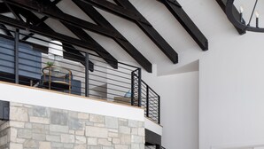 A spacious living area with a stone fireplace, wooden furniture, and a mezzanine level with a balcony. - Sweeping Teton views, modern renovation. Minutes from town & National Parks. (Jackson)