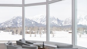 A modern living room with large windows, a fireplace, and a view of snow-covered mountains. - Sweeping Teton views, modern renovation. Minutes from town & National Parks. (Jackson)
