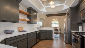 A modern kitchen with dark cabinetry, a central island, and stainless steel appliances. - Incredible home with custom pool and fountain (El Paso)