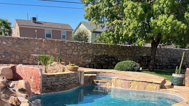A clear blue swimming pool with a stone wall and a small waterfall feature. - Incredible home with custom pool and fountain (El Paso)