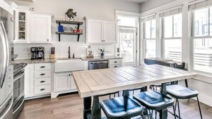 A modern kitchen with white cabinetry, a wooden dining table, and bar stools.