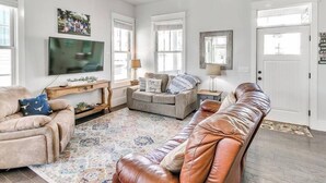 A living room with a sofa, a television, a ceiling fan, and a door.