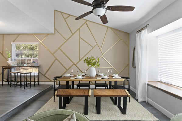 A dining area with a geometric wall design, a ceiling fan, and a window with blinds.