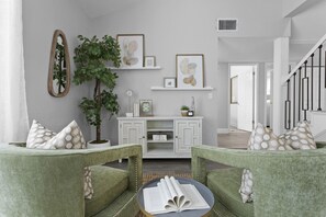 A modern living room with green upholstered chairs, a white console table, and a large plant.