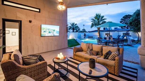 A modern living room with a sofa, chairs, a coffee table, and a TV. There is a pool area visible through the glass door. - The White House, Heated Pool! PuttingGreen (Phoenix)
