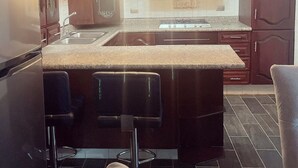 Een moderne keuken met donkere houten kasten, een granieten aanrecht en een centraal keukenblok met barstoelen.