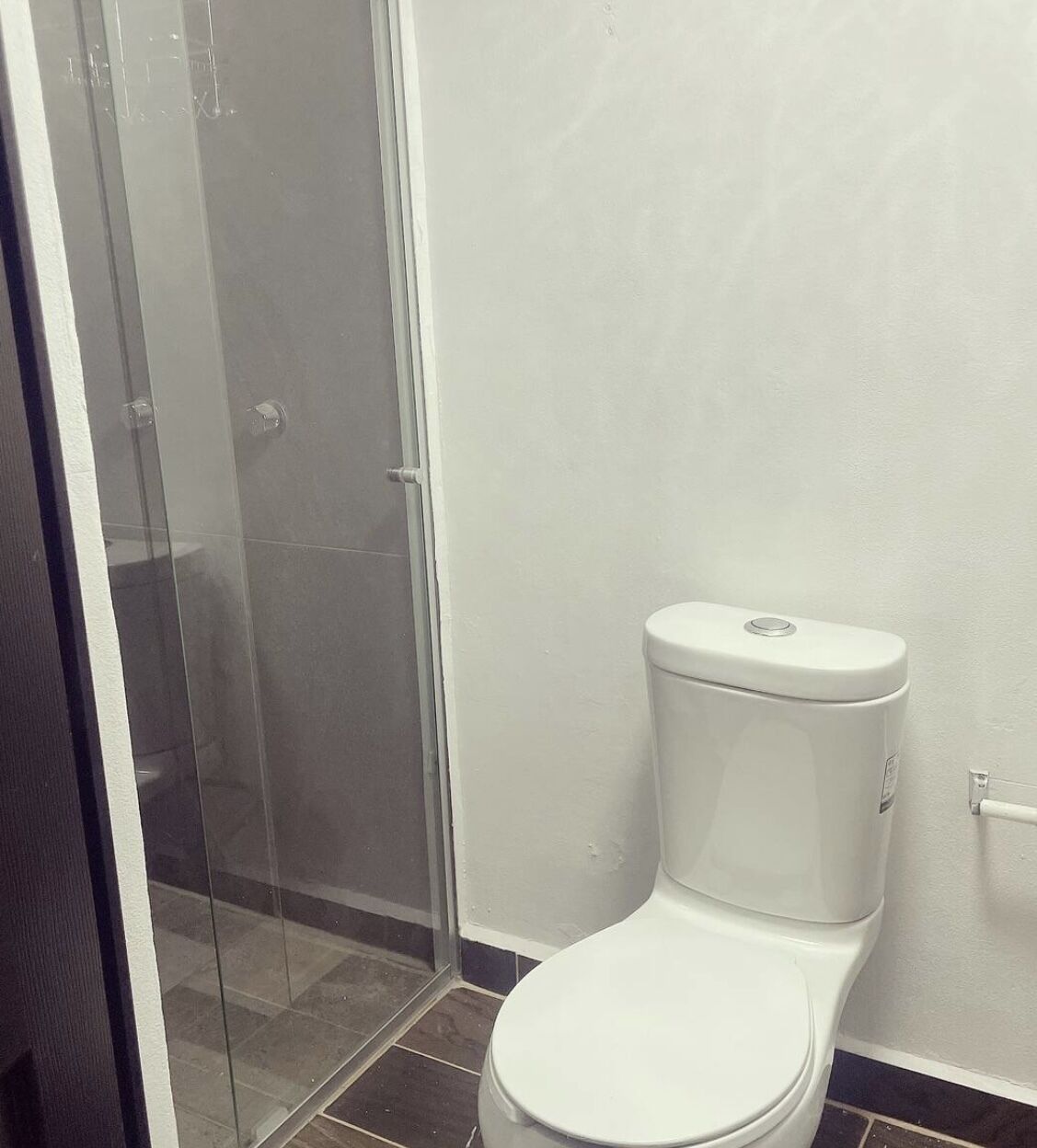 A bathroom with a white toilet, a glass shower enclosure, and a tiled floor.
