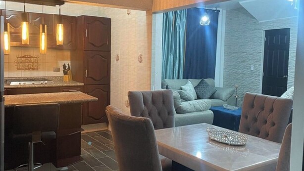 Een moderne keuken met een bar, een eettafel met stoelen, en een gezellige zithoek met een bank en gordijnen.