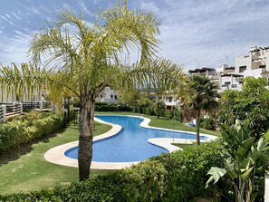 Une piscine au design incurvé, entourée d’une végétation luxuriante et de palmiers.