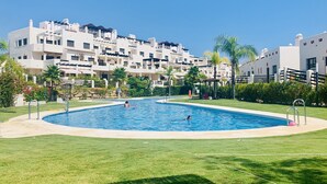 Una piscina rodeada de un césped cuidado, con edificios de varios pisos al fondo.