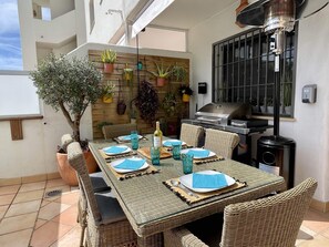 An outdoor dining area with wicker furniture, a table set for four, and a variety of potted plants on a wall. - Cozy Apartment with a Swimming Pool (Estepona)