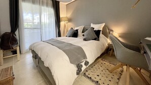 Un dormitorio ordenado con cama, mesitas de noche, un escritorio y una silla.
