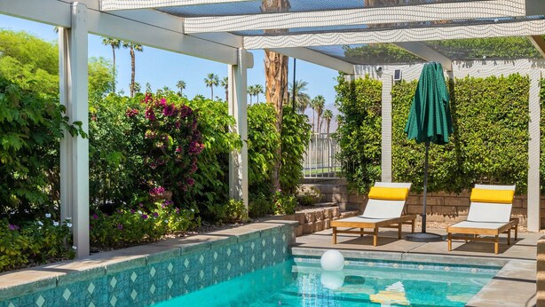A clear blue pool with a tiled edge, surrounded by a covered area with two lounge chairs and a green umbrella. - Golf Course Villa, Private Saltwater Pool & Spa (Indio)