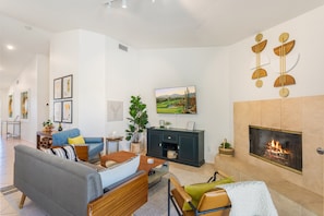A modern living room with a fireplace, a sofa set, a dining table, and a TV mounted on the wall. - Golf Course Villa, Private Saltwater Pool & Spa (Indio)