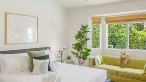 A modern bedroom with a bed, green sofa, and a large window with a view of greenery. - Golf Course Villa, Private Saltwater Pool & Spa (Indio)