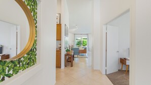 A hallway with a large mirror, a wooden cabinet, a small table with a plant, and a view of a living area with a blue chair and a desk. - Golf Course Villa, Private Saltwater Pool & Spa (Indio)