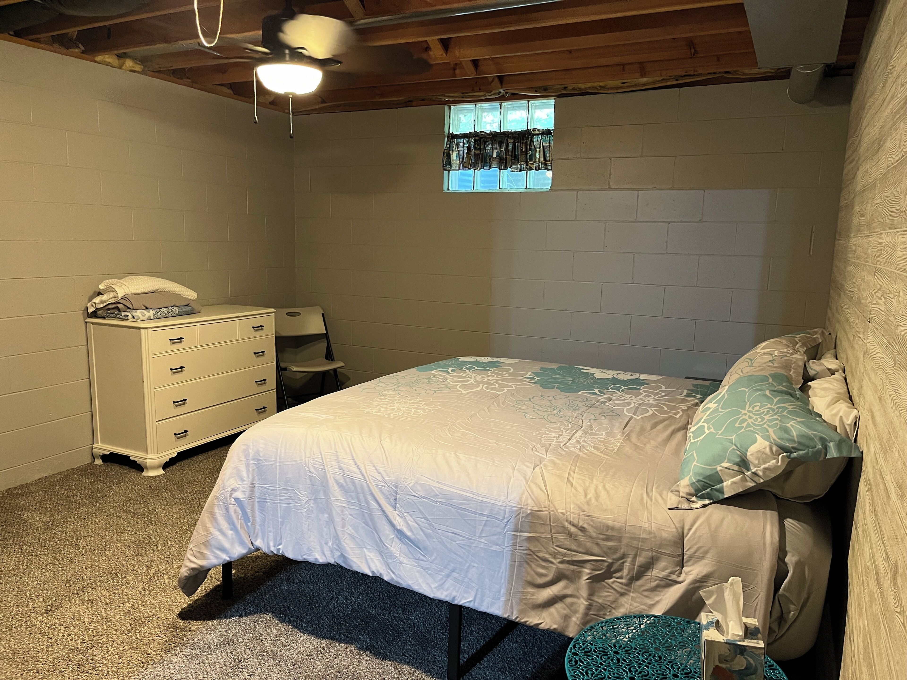 A bedroom with a bed, dresser, chair, and a small window.