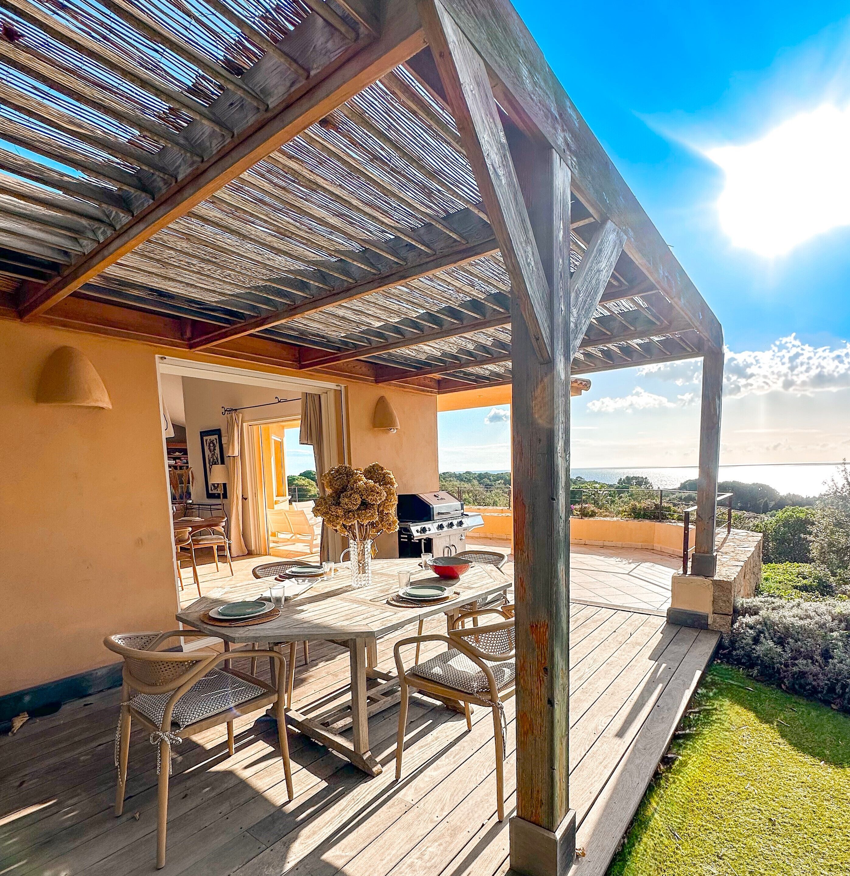 Een terras buiten met een houten tafel en stoelen, een barbecue en uitzicht op het landschap.