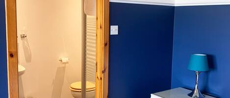 A bedroom with a wooden door leading to a bathroom, a bedside table with a lamp, and a bed with white bedding.