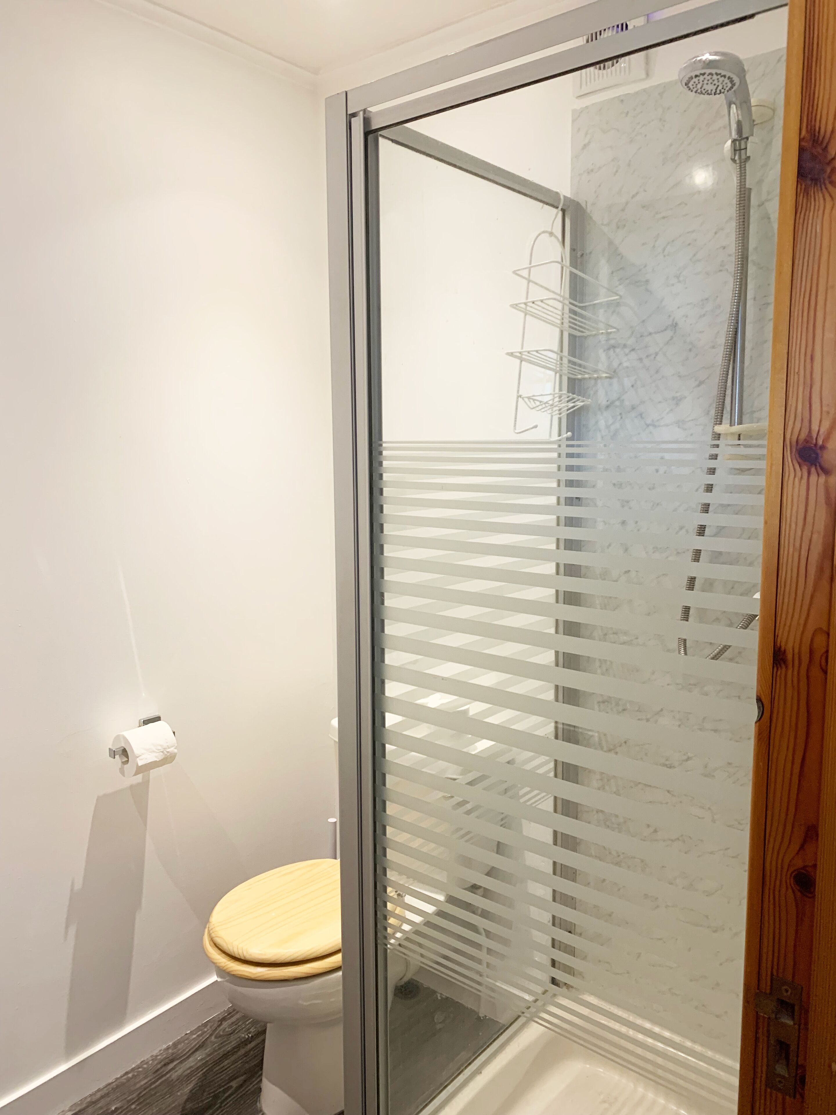 Et moderne badeværelse med en glasbrusekabine, toilet og en marmorbeklædt væg.