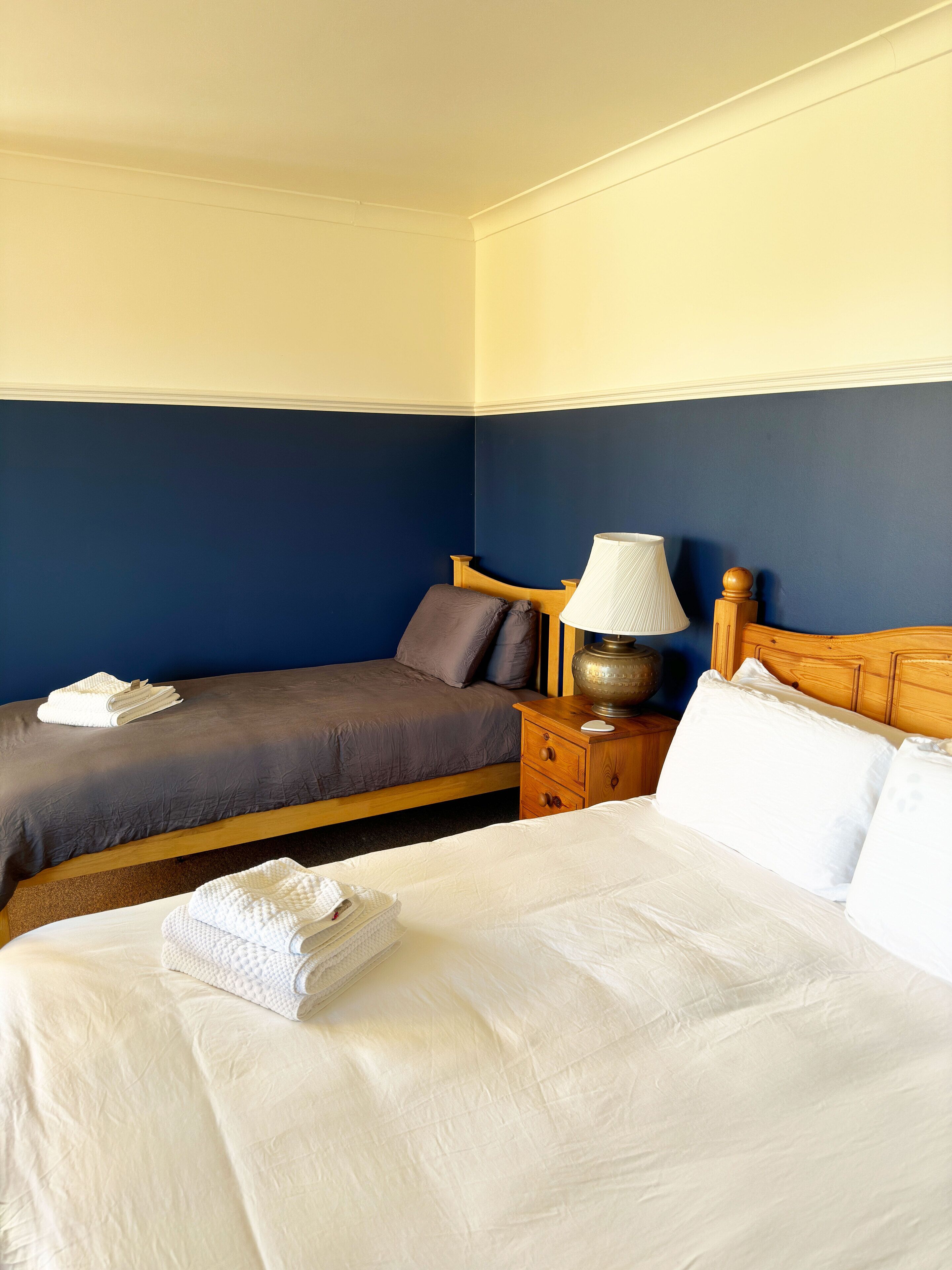 A hotel room with two beds, a nightstand with a lamp, and a wooden headboard.